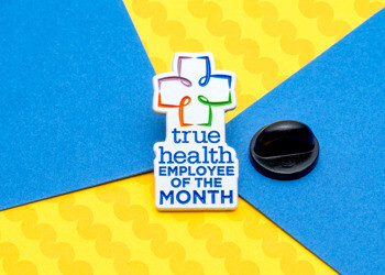 True Health Employee of the Month lapel pin with a colorful cross logo and blue text on a white background.